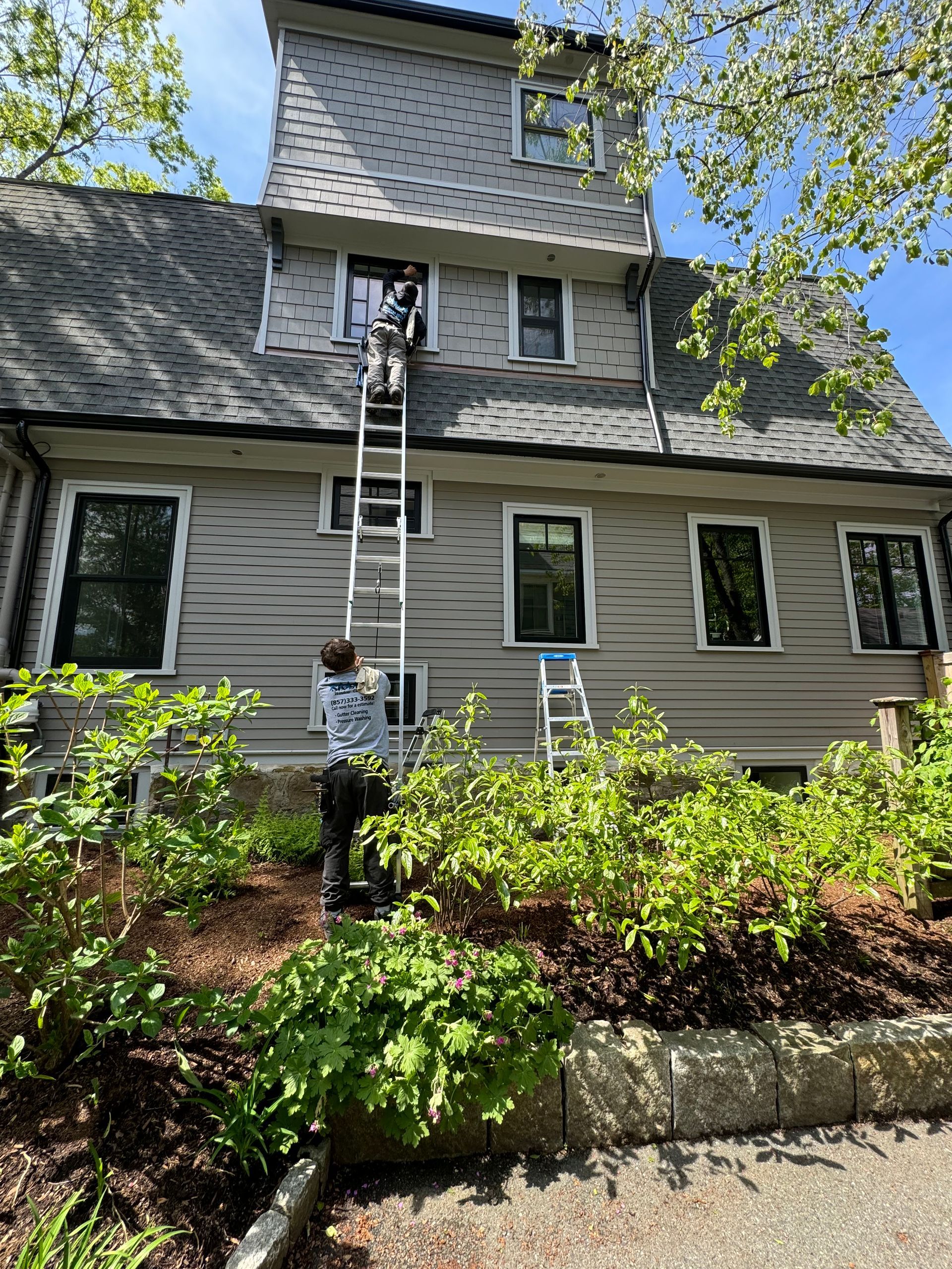 A man is standing on a ladder painting the side of a house.