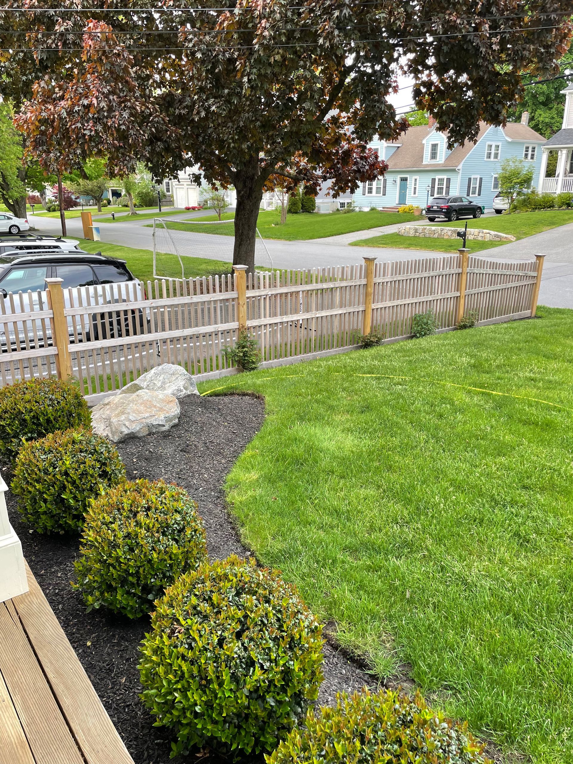 A wooden fence surrounds a lush green lawn in a residential neighborhood.