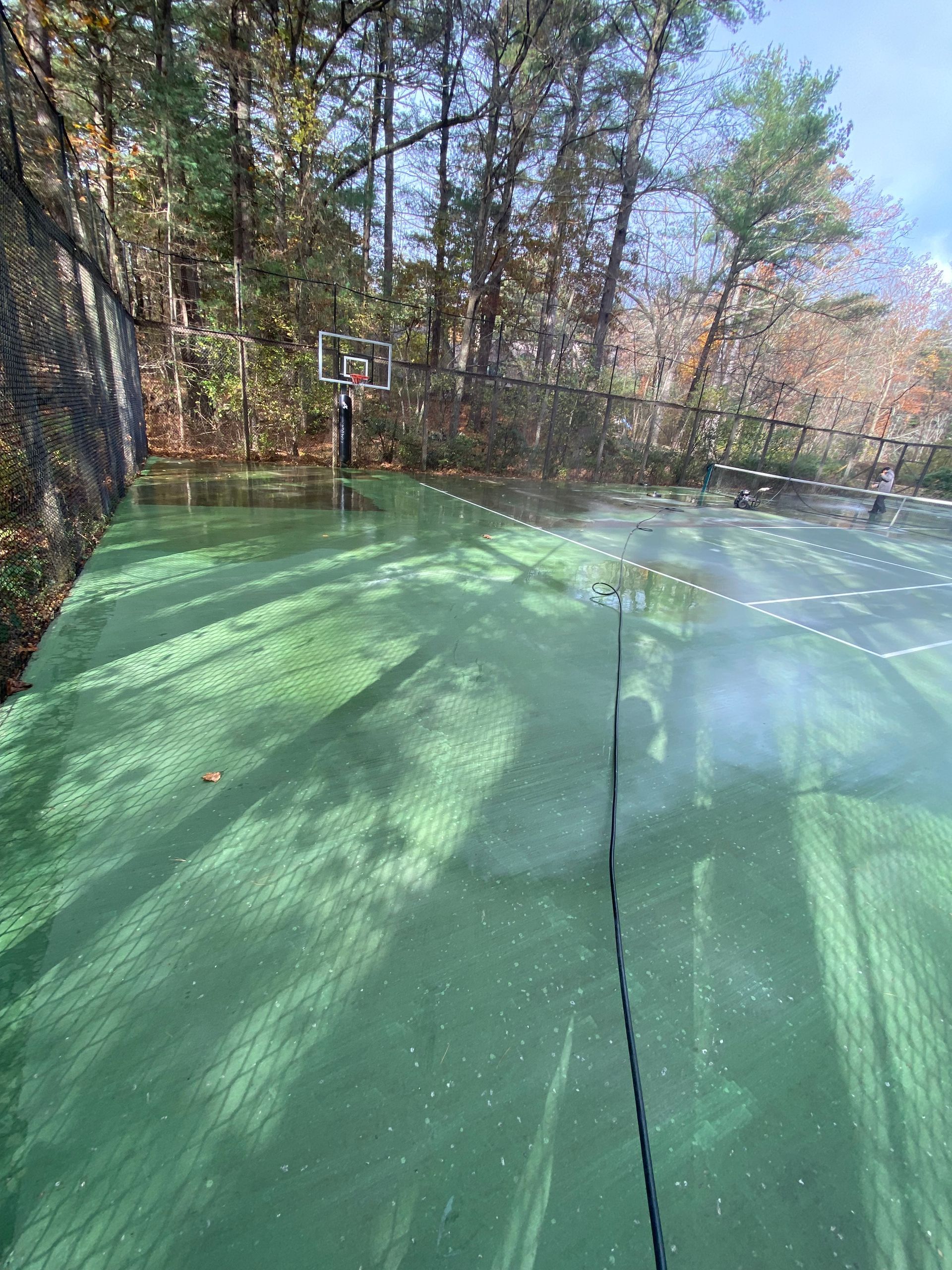 A green basketball court surrounded by trees on a sunny day.