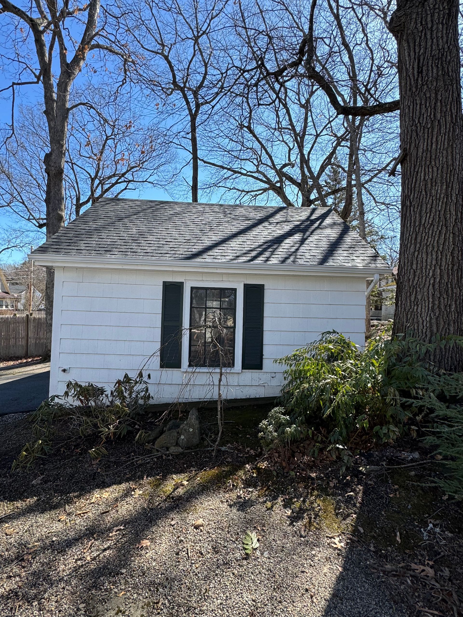 A small white house with black shutters is sitting next to a tree.