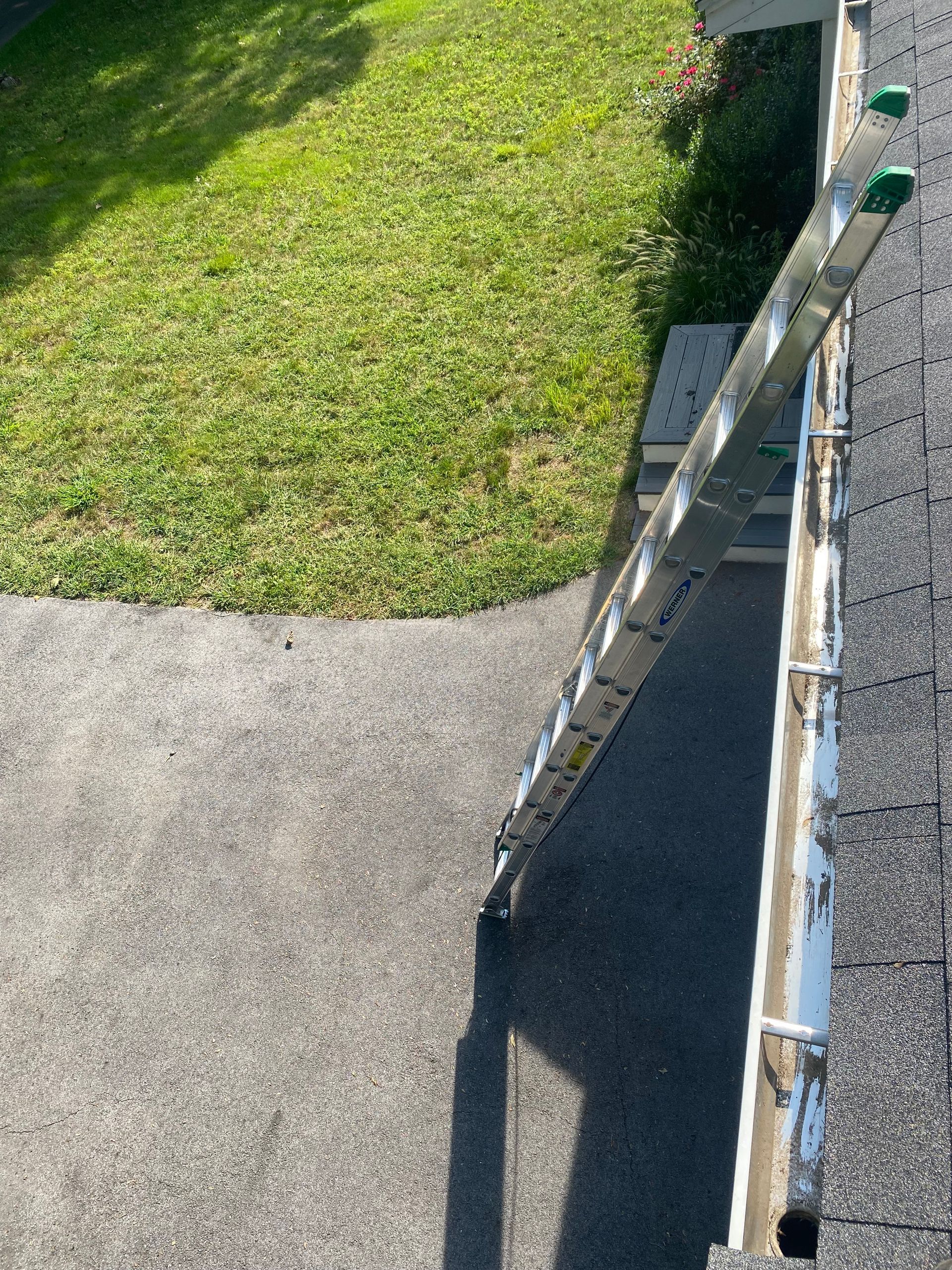 A ladder is sitting on top of a roof next to a grassy area.