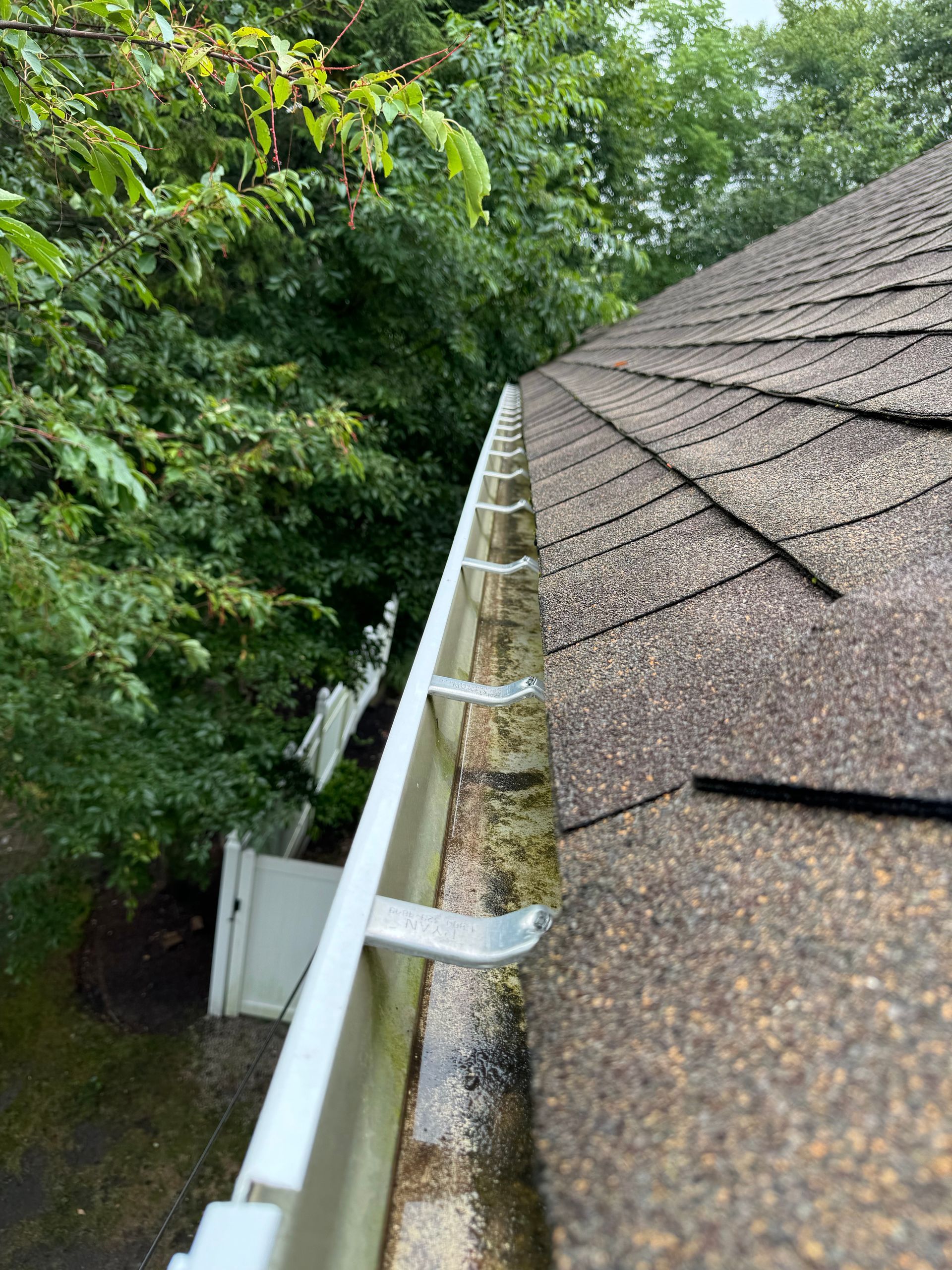 A close up of a gutter on a roof with trees in the background.