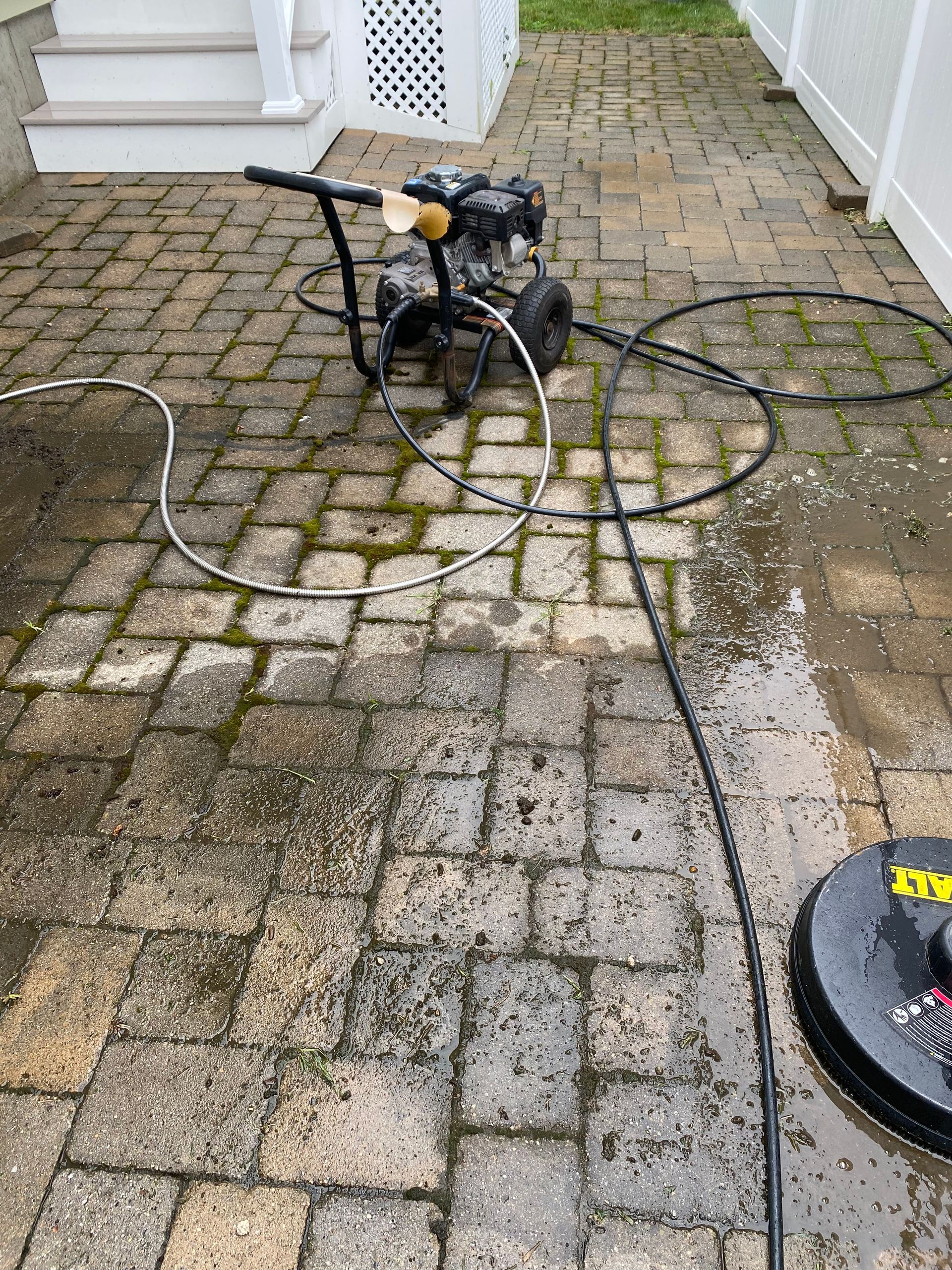 A pressure washer is being used to clean a brick walkway.