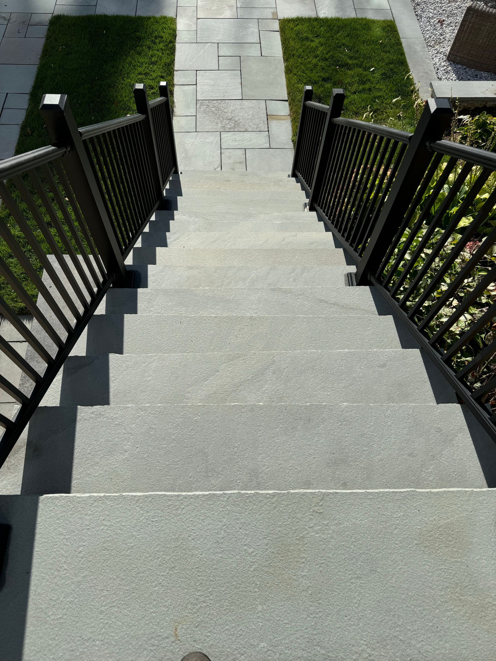 A set of stairs with a black railing leading up to a grassy area.