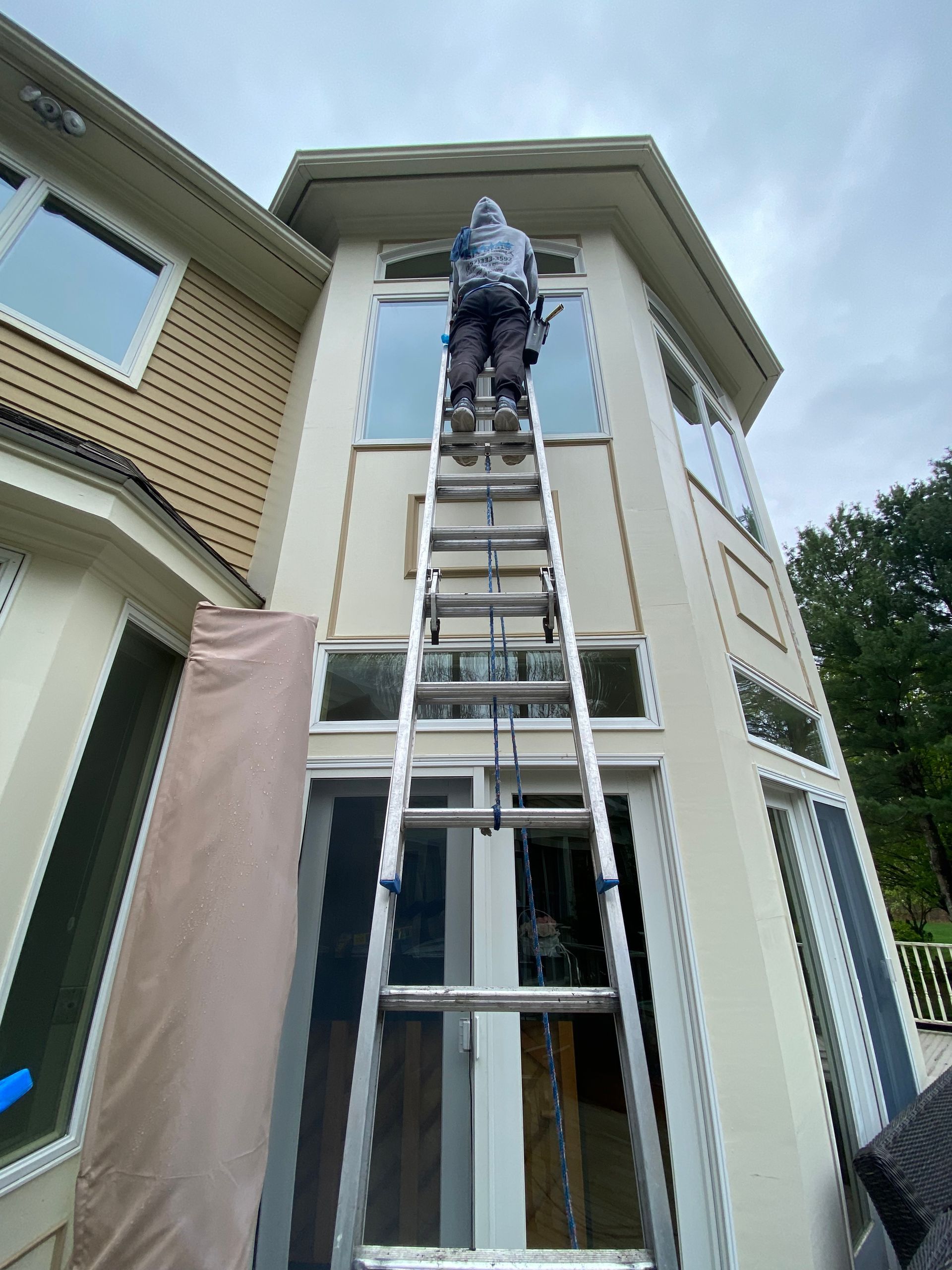 A man is standing on a ladder on the side of a house.