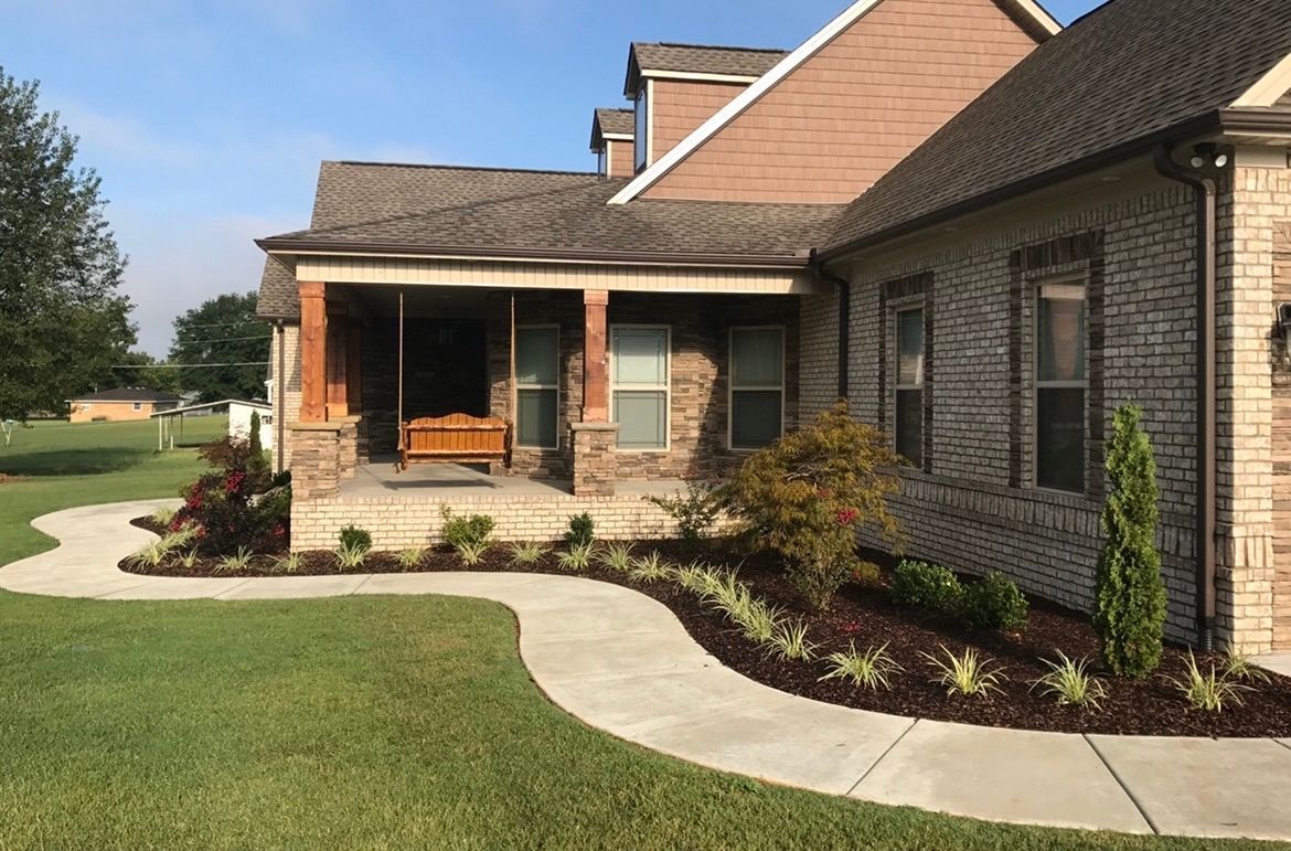 A brick house with a porch and a concrete walkway leading to it