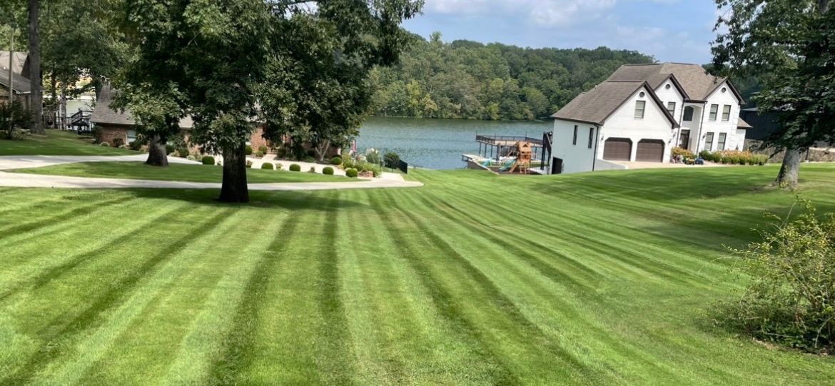 A lush green lawn with a house in the background and a lake in the background