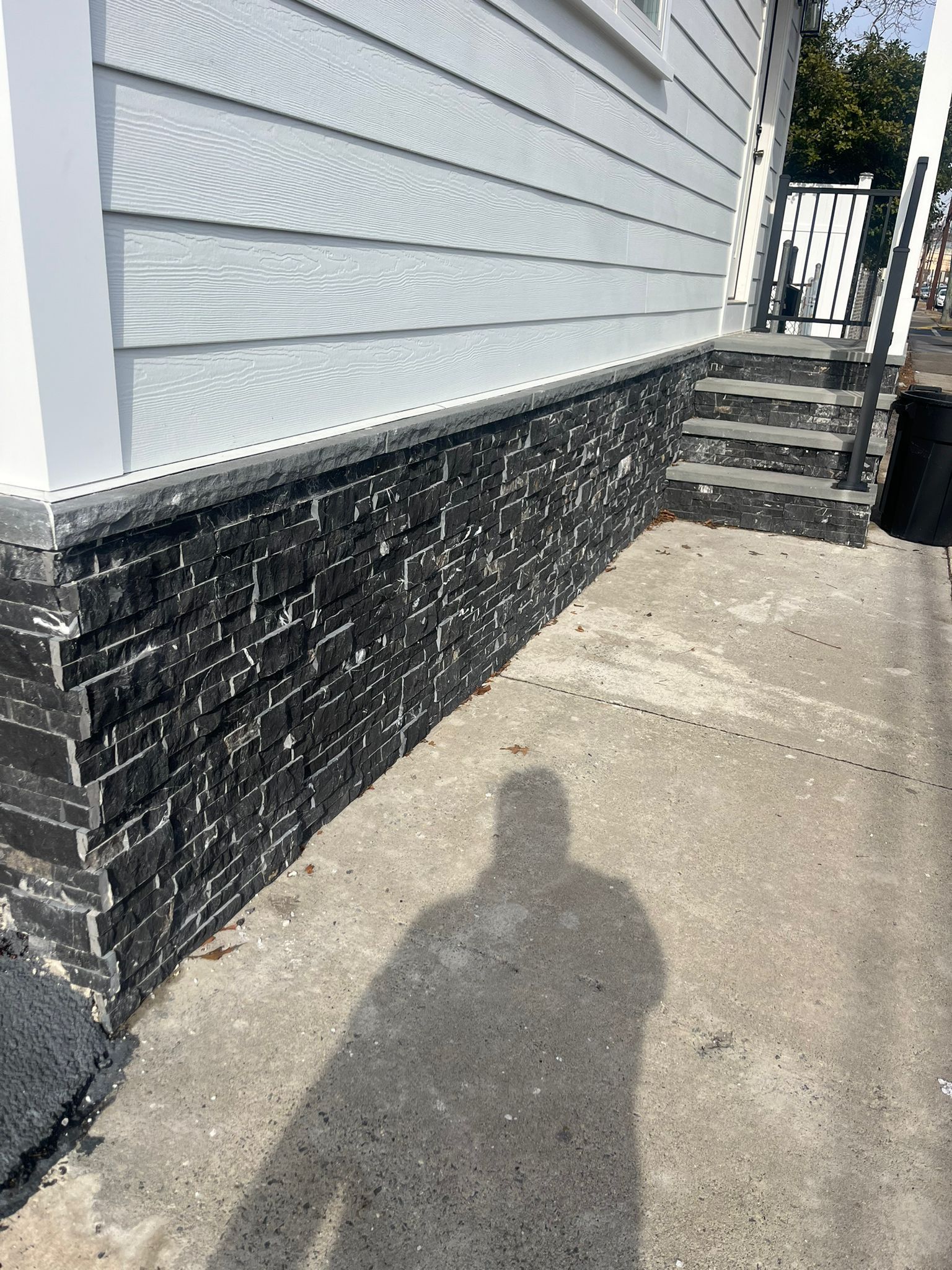 A shadow of a person is cast on the sidewalk in front of a house.