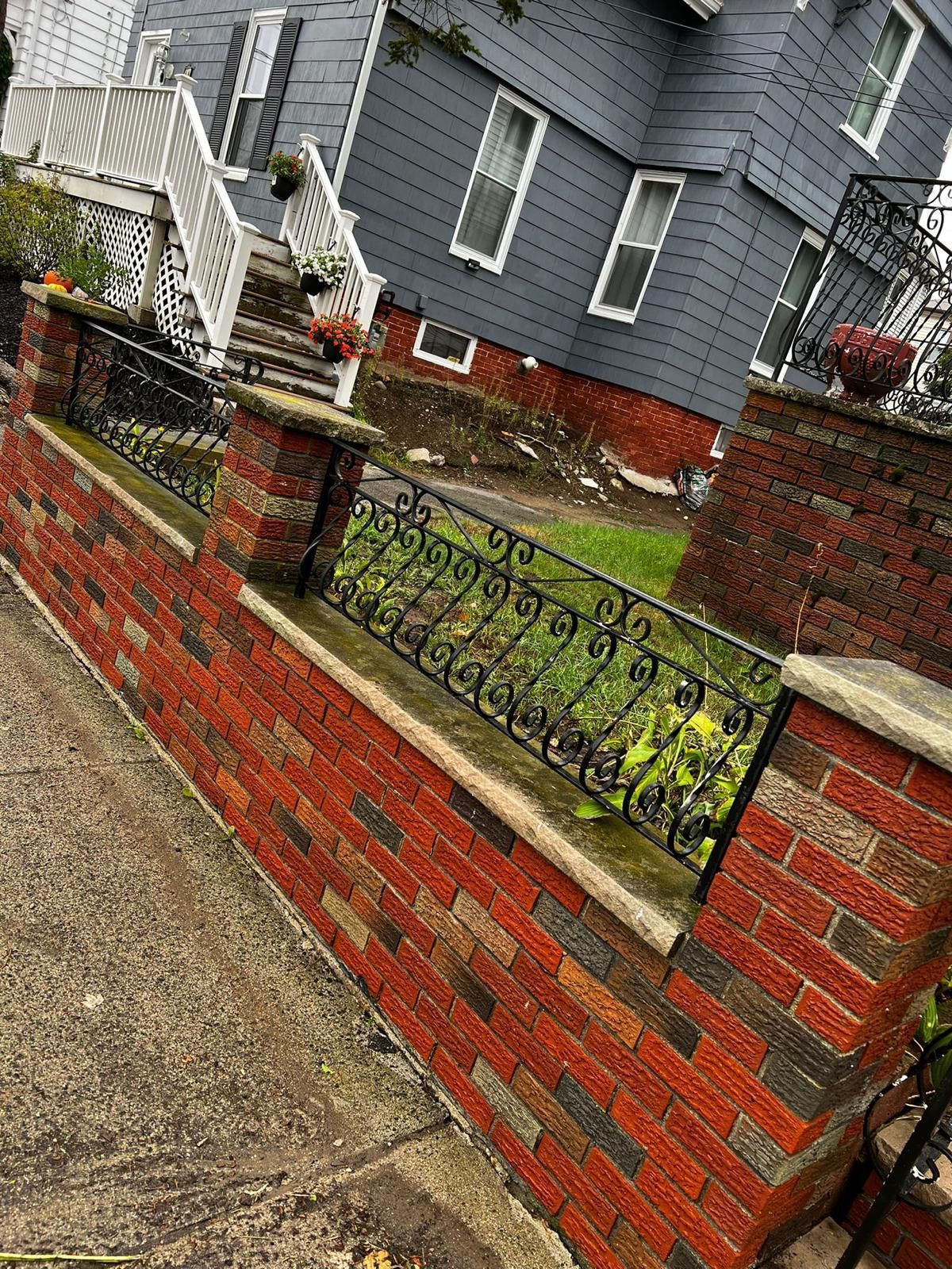 A brick wall with a wrought iron fence in front of a house.