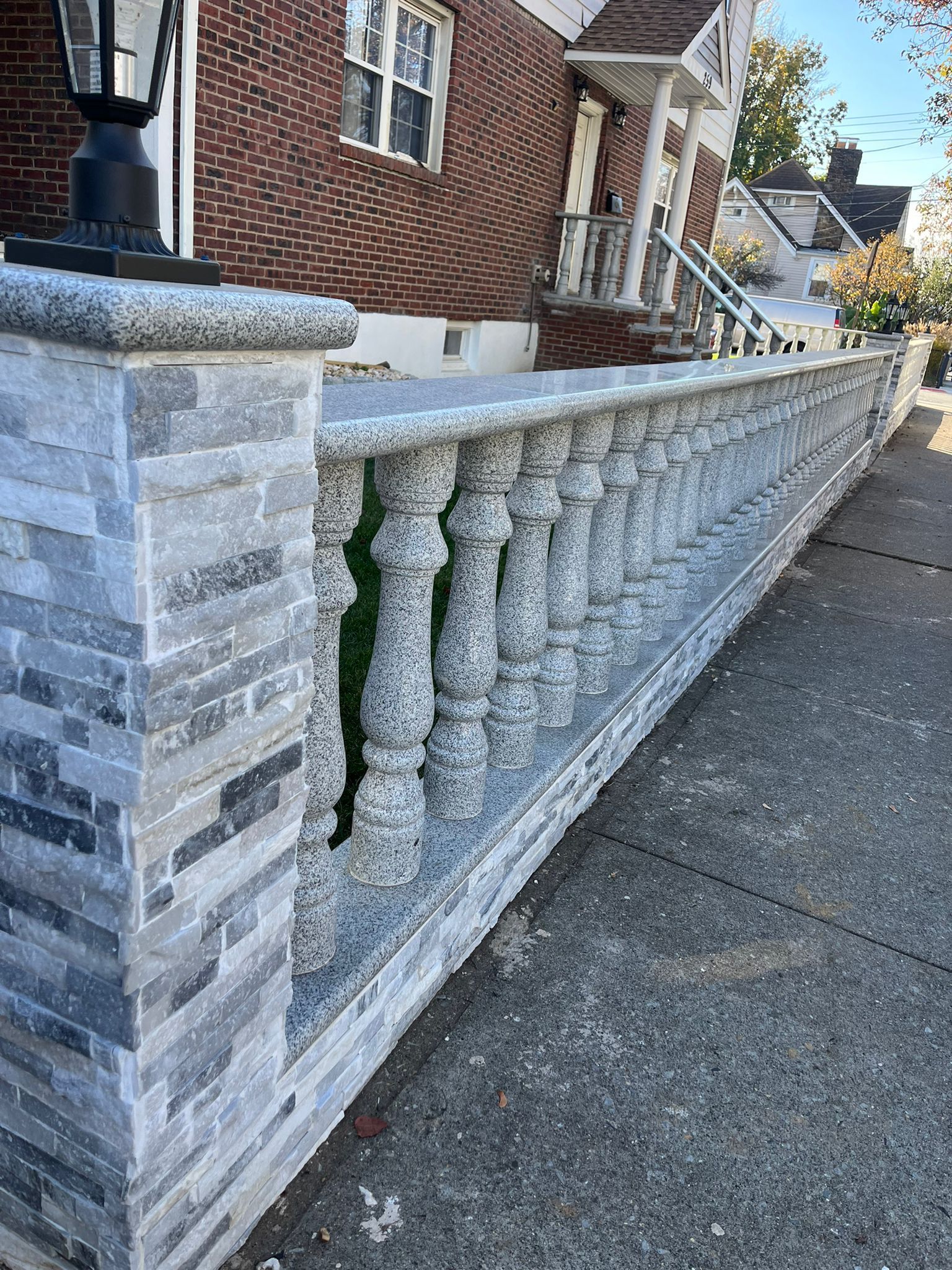 A stone wall with a railing in front of a brick house.