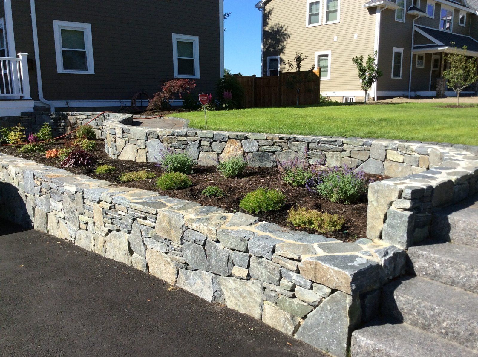 A stone wall with a garden in front of a house