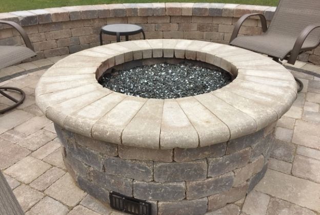 A fire pit is sitting on a patio next to chairs.