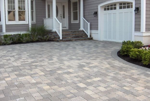 A brick driveway in front of a house with a white garage door.