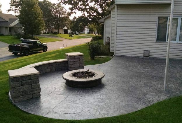 A fire pit is sitting on a concrete patio in front of a house.