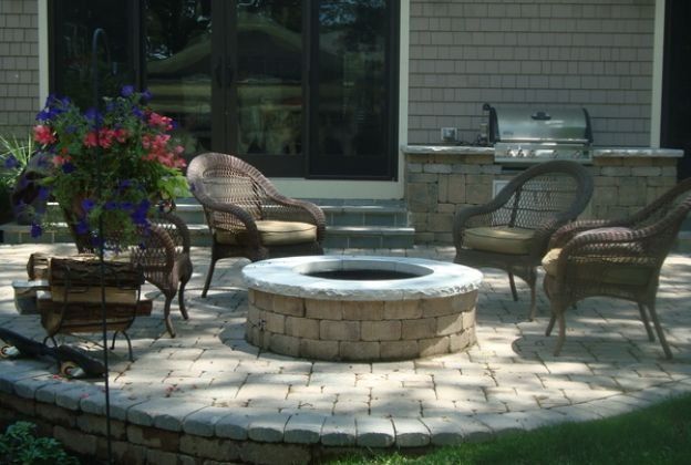 A fire pit on a patio with chairs and a grill.