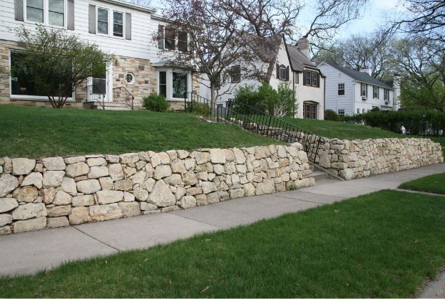 A stone wall along the sidewalk in front of a house