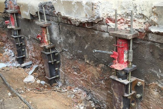 A group of hydraulic jacks are sitting in the dirt next to a brick wall.
