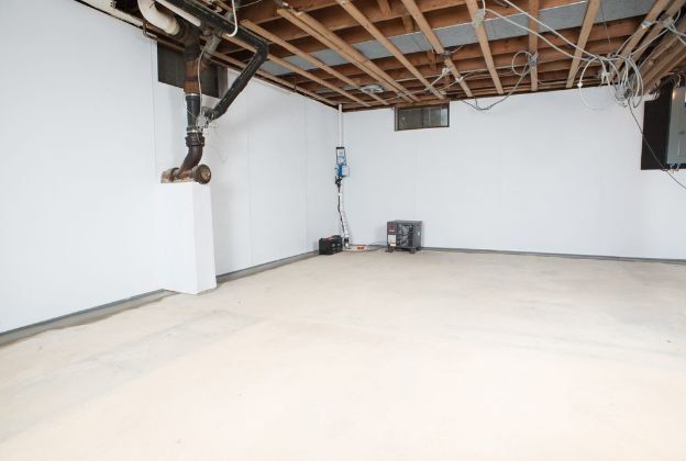 An empty basement with white walls and a wooden ceiling.