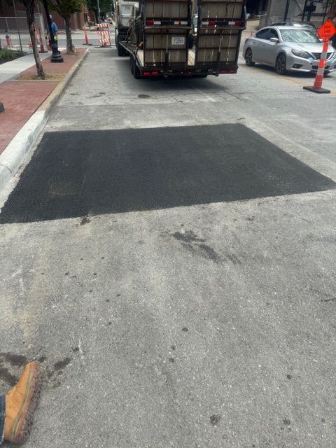 A truck is driving down a street next to a patch of asphalt.