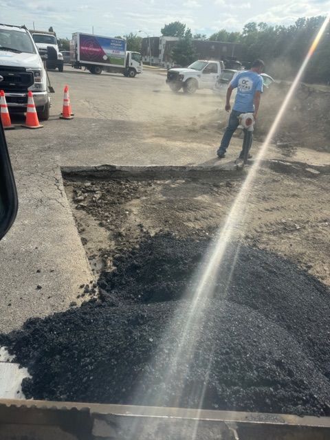 A man is pouring asphalt into a hole in the ground.