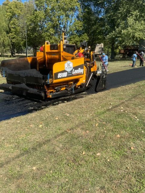 A yellow tractor is laying asphalt in a park.