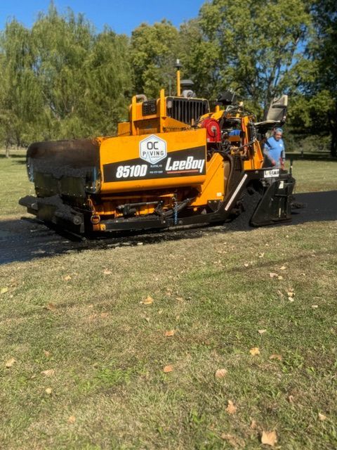 A yellow and black asphalt paving machine is parked in a grassy field.