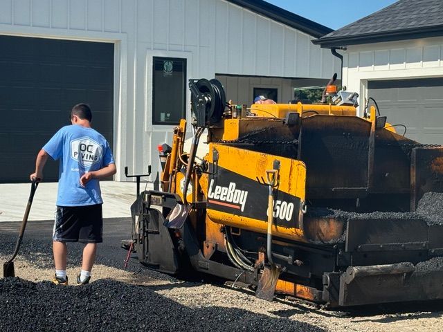 A man is standing next to a machine that is laying asphalt.