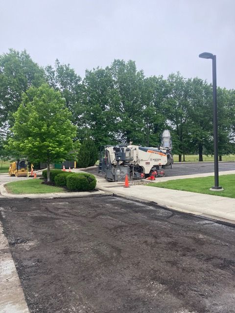 A machine is cutting asphalt in a parking lot