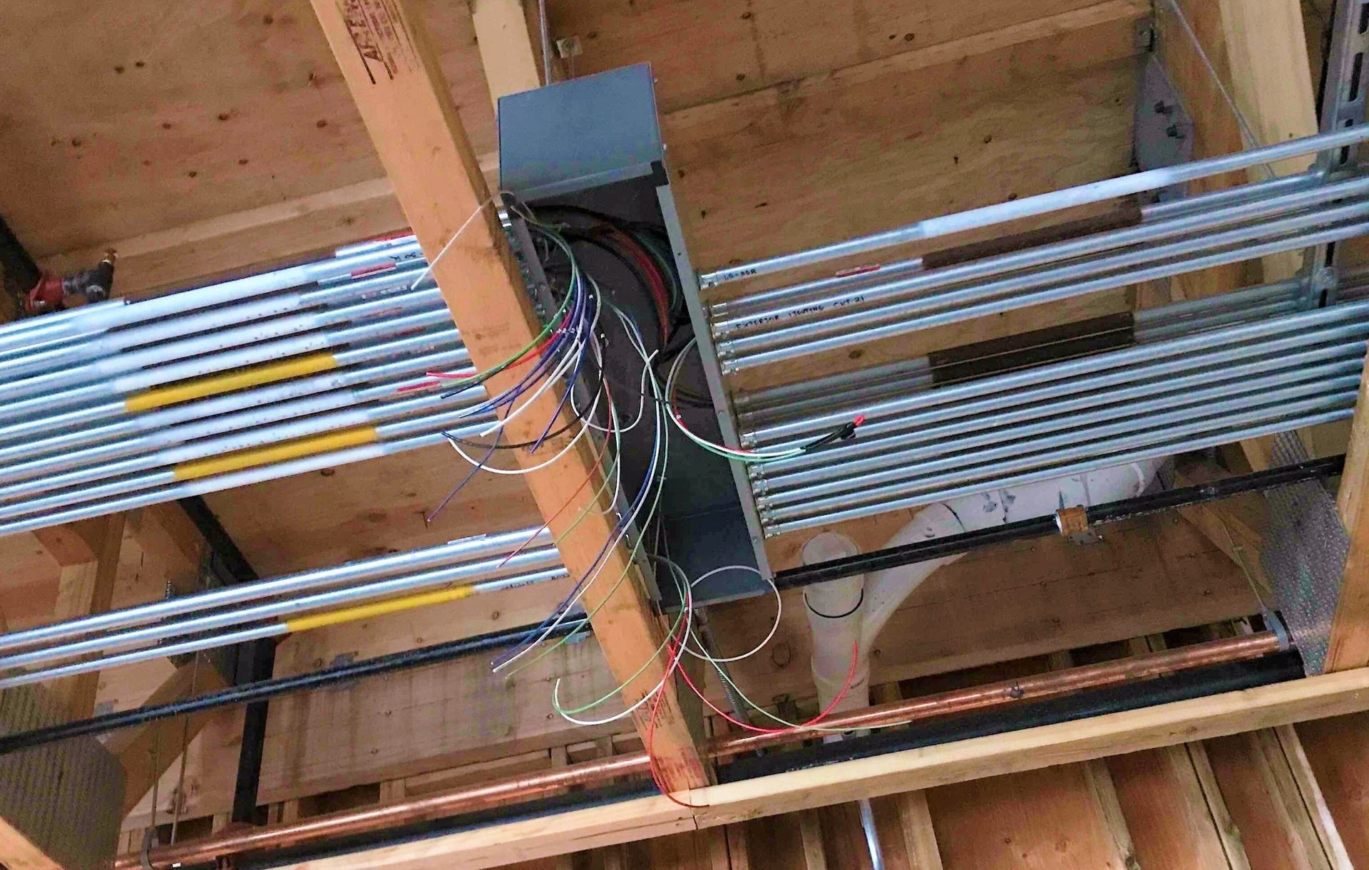 Electrical conduit and wiring mounted on exposed wooden ceiling beams during construction.