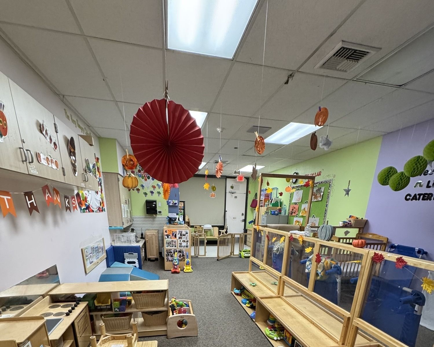 Colorful classroom with hanging paper decorations, tables, shelves, and play materials.