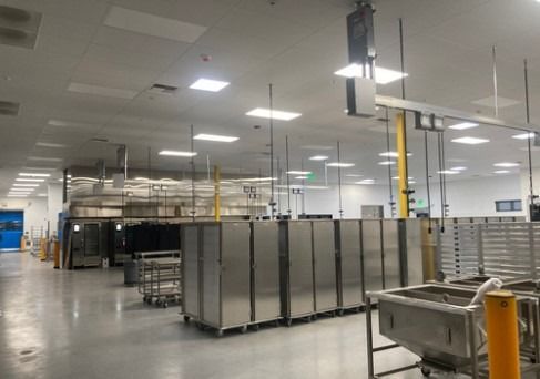 Industrial warehouse interior with stainless steel equipment and storage racks under bright ceiling lights