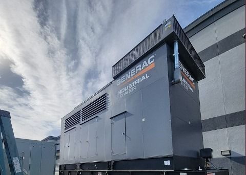 Large gray industrial generator unit beside a building under a cloudy sky