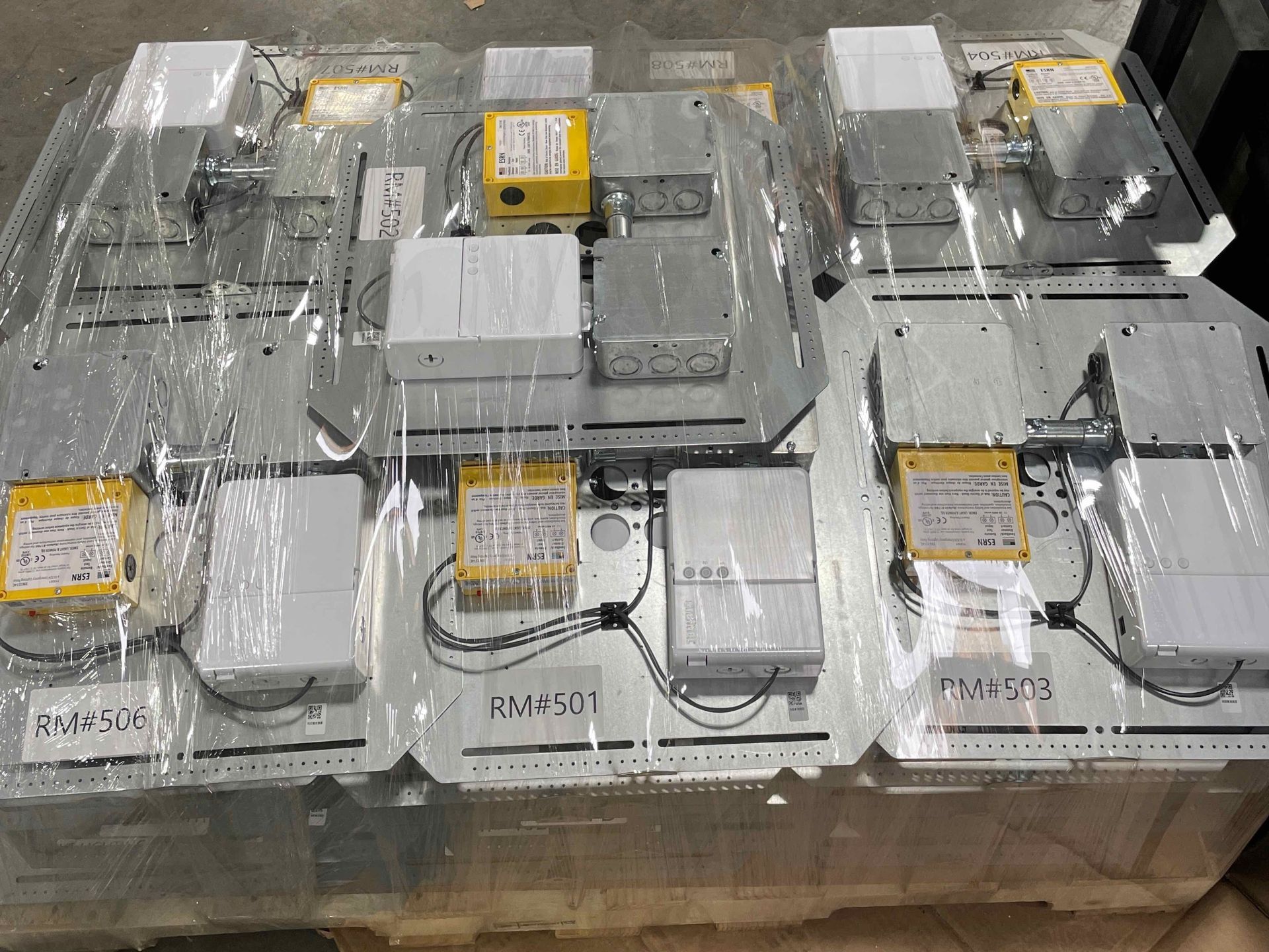 Pallet of packaged white and gray electronic devices wrapped in plastic and stacked for shipping