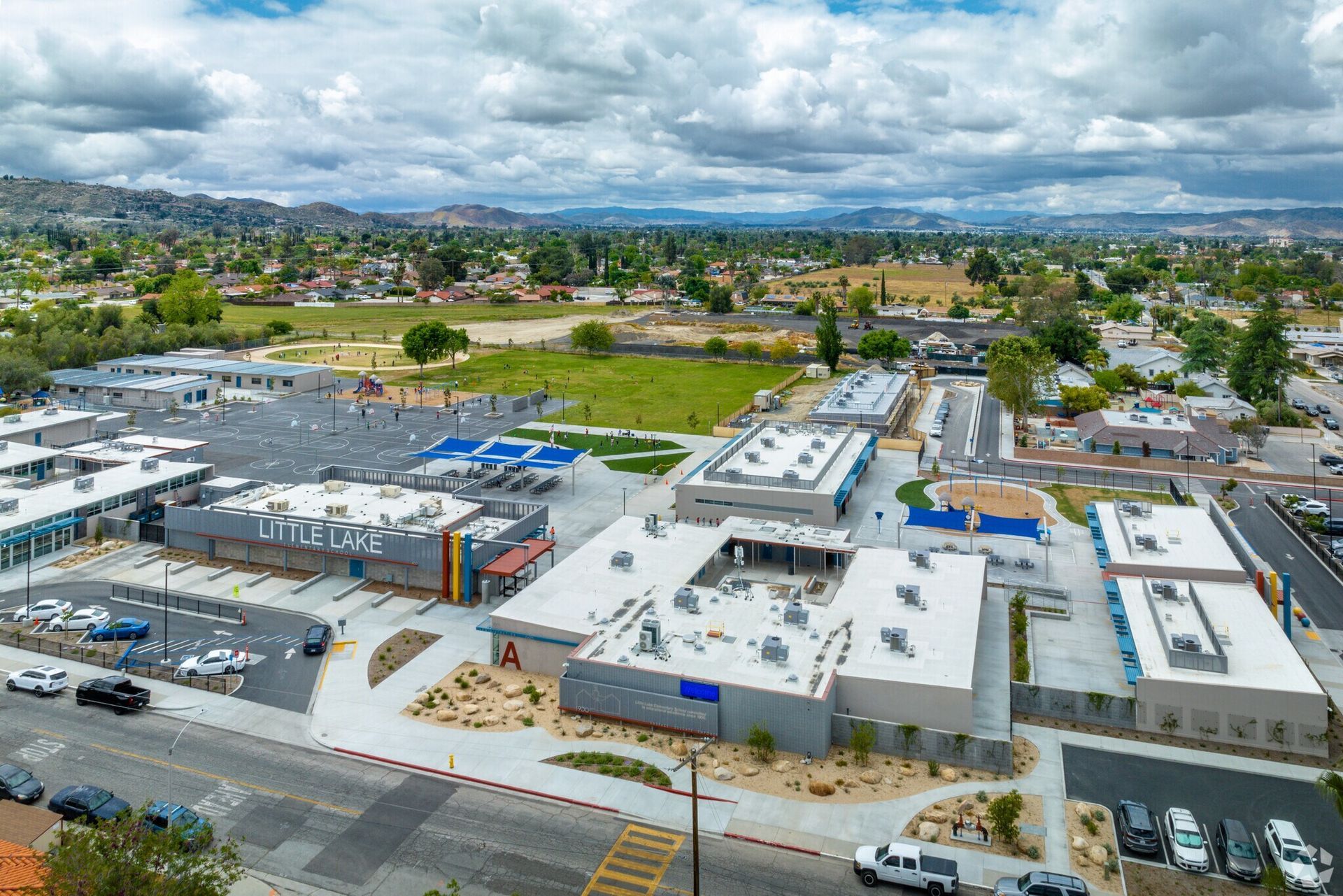 Aerial view of a commercial plaza with parking lots, stores, and a cloudy sky over a suburban area