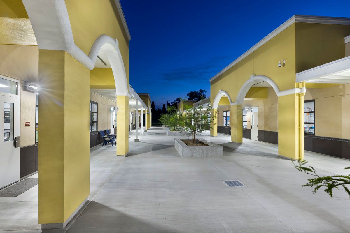 Yellow courtyard walkway at dusk with arches, benches, and a blue sky