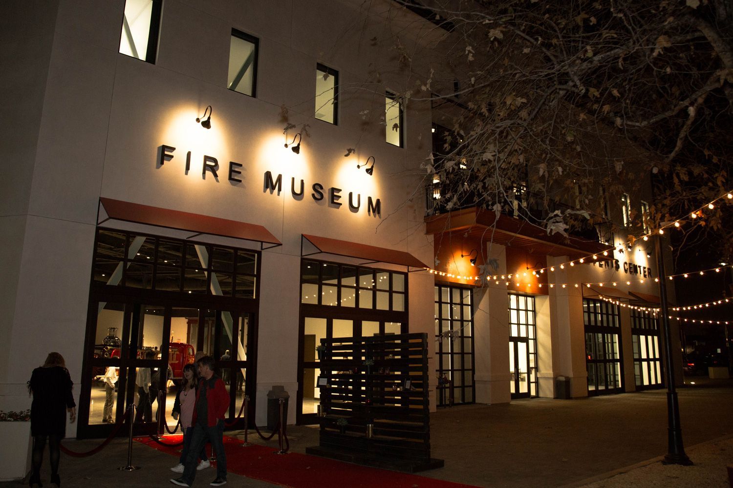 Nighttime exterior of the Fire Museum with lit windows, red carpet entrance, and string lights.