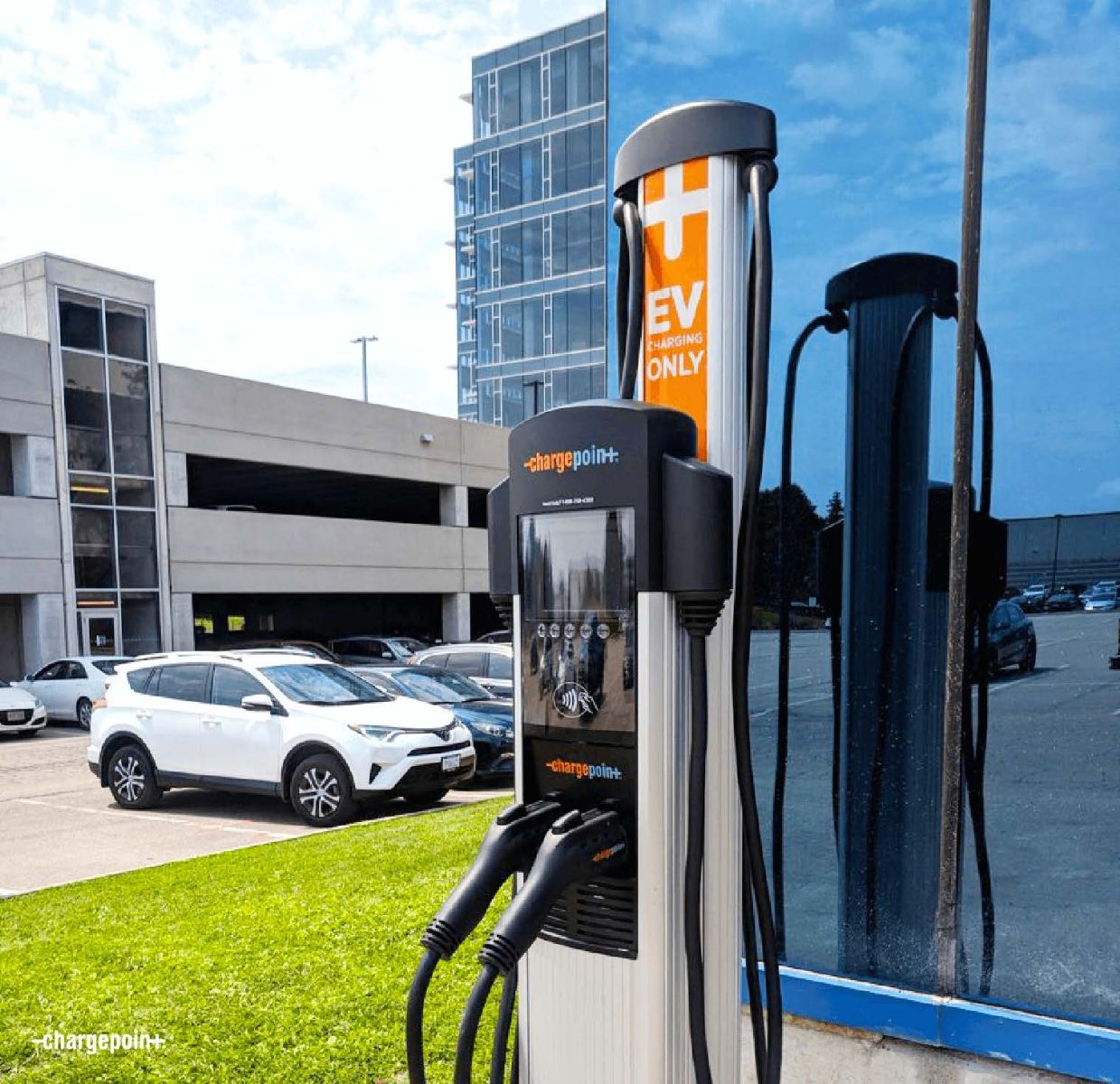 EVgo electric vehicle charging station outside a parking garage, with cars parked nearby.