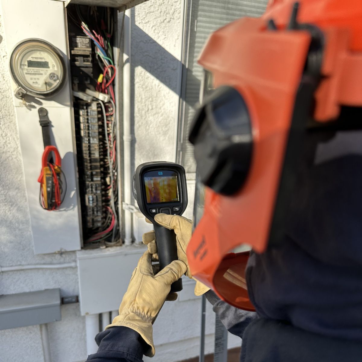 Technician using a thermal camera to inspect an open electrical panel outdoors