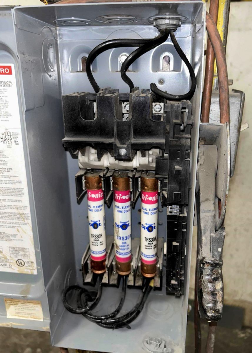 Open electrical panel with three colored fuse cartridges and wiring inside a gray metal box