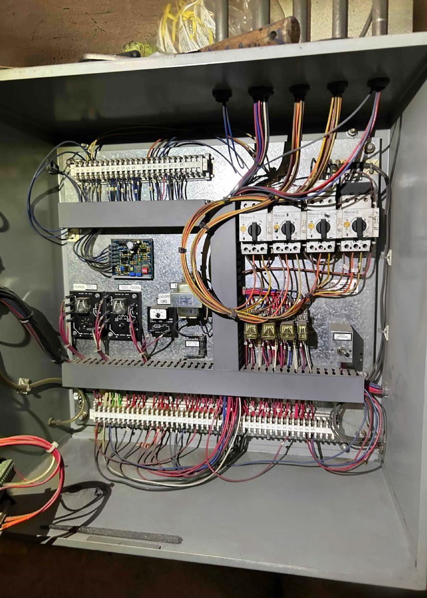 Open electrical control panel with wiring, relays, and circuit breakers on a gray metal cabinet