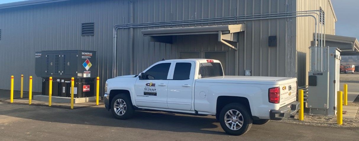 White pickup truck parked beside a metal building with yellow bollards and industrial equipment.