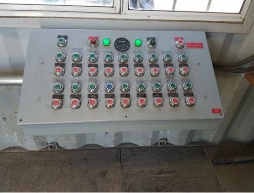 Industrial control panel with rows of red and green buttons, mounted below a window.