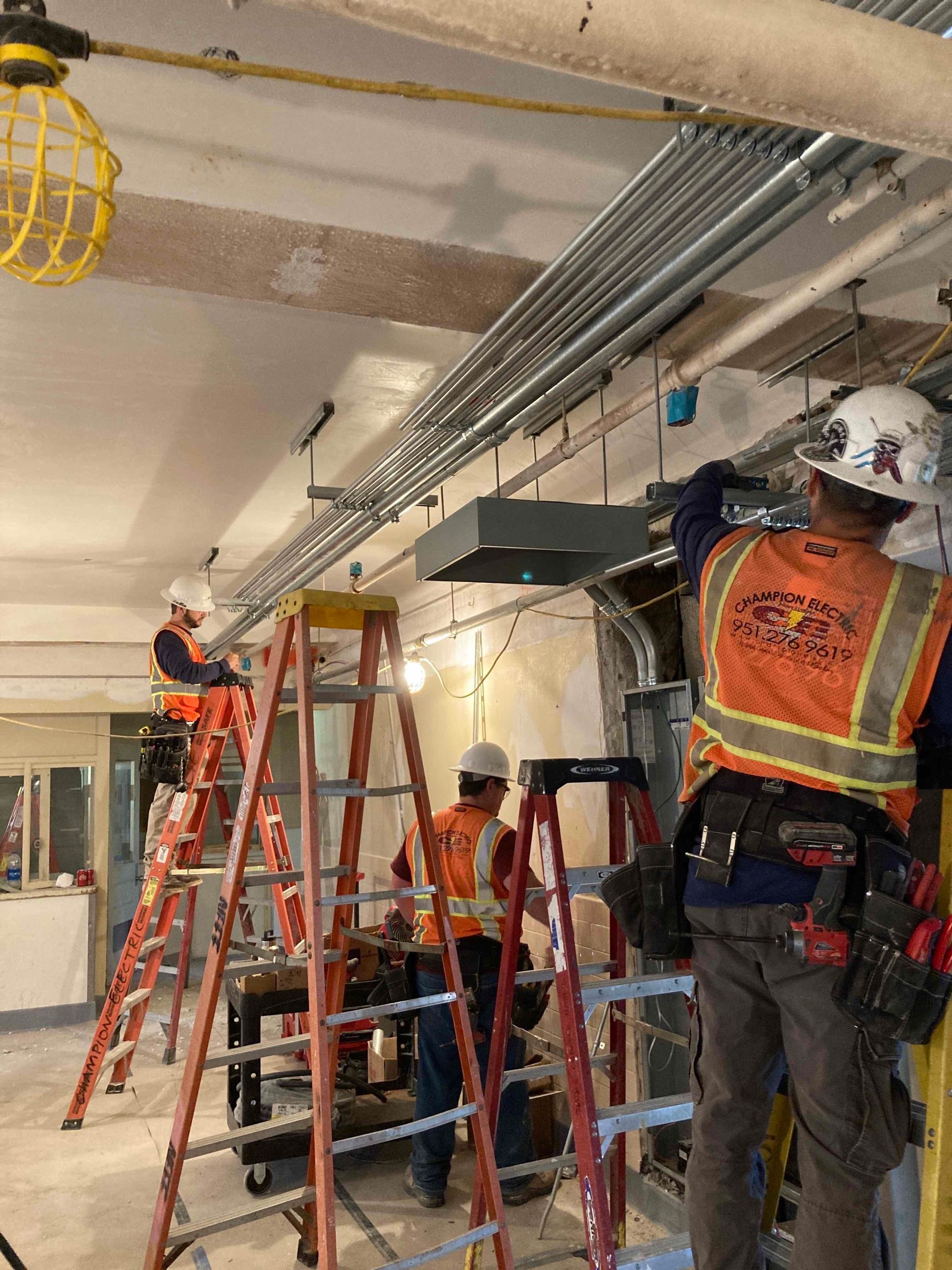 Workers on ladders and scaffold installing overhead pipes in a construction area