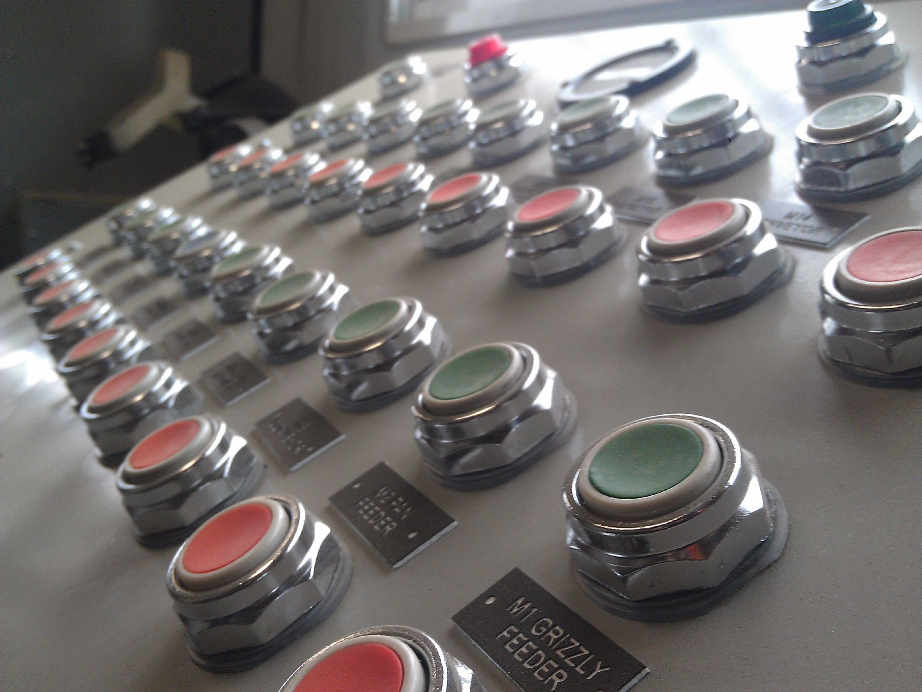 Row of illuminated metal push buttons on a control panel, viewed at an angle.