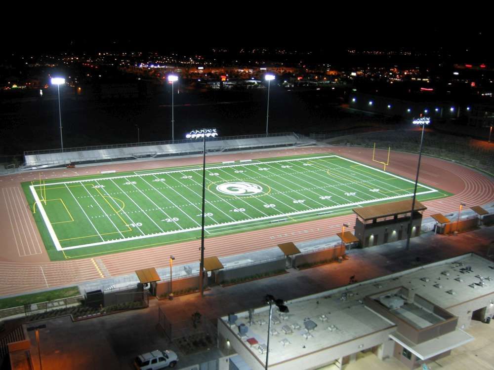 Nighttime view of a lit green football field with bleachers and surrounding track at a stadium