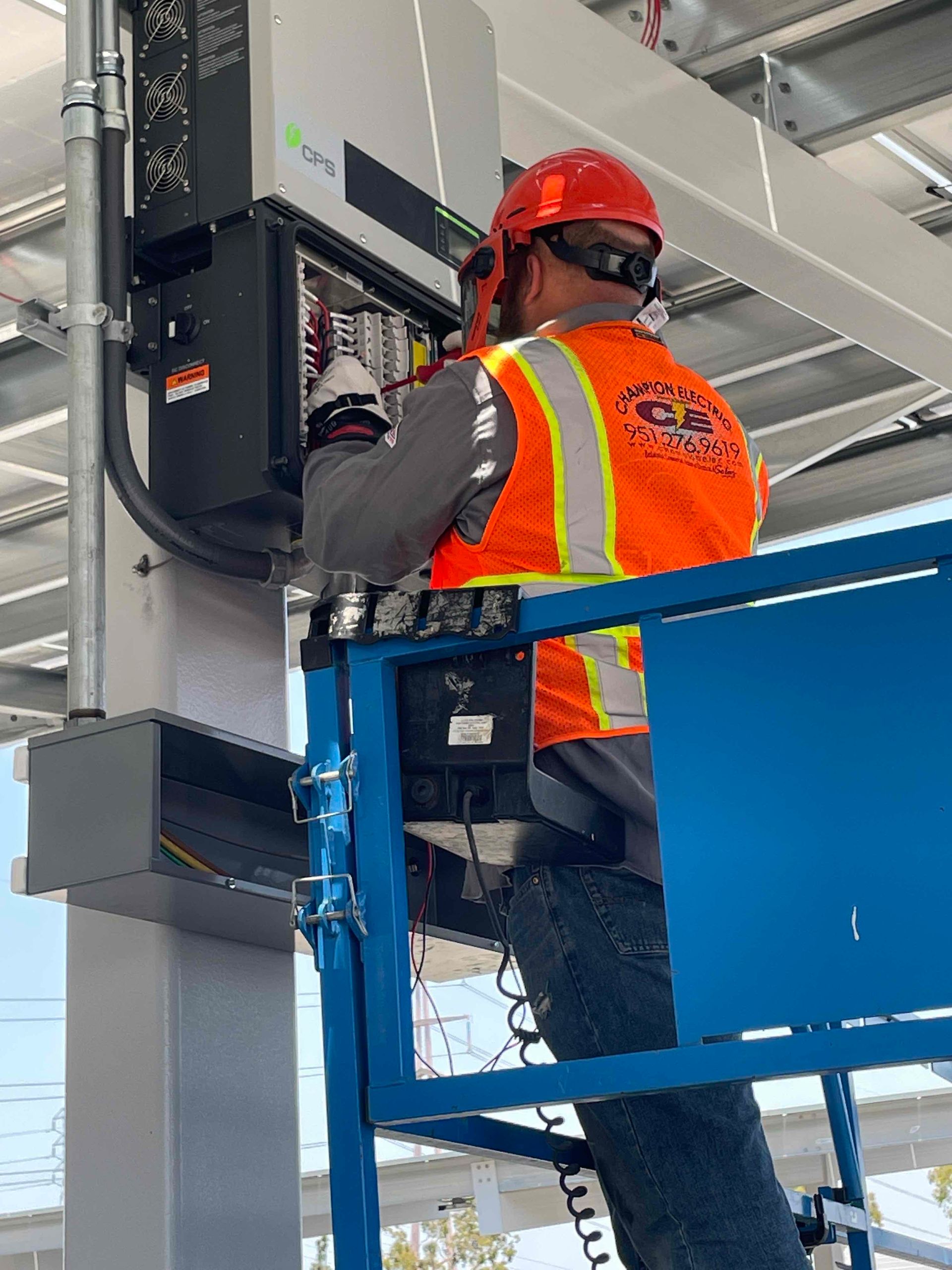 Worker in orange safety vest and hard hat servicing equipment on a raised platform.