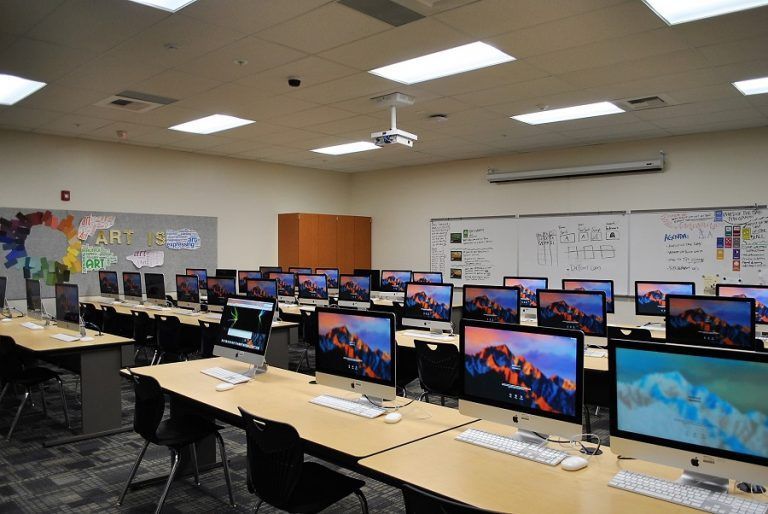 Computer lab with rows of desktop monitors and desks under bright ceiling lights