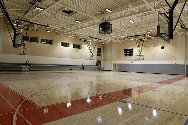 Empty indoor basketball court with polished wooden floor, hoops, bleachers, and overhead lights