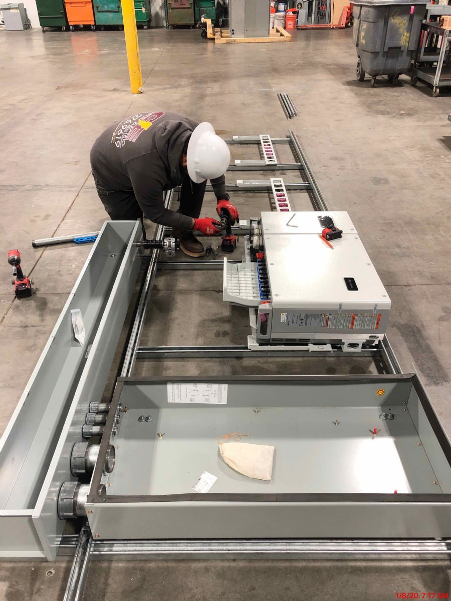 Worker assembling a metal frame beside a control box in an industrial workshop