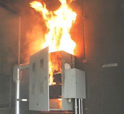 Industrial machine engulfed in flames, with bright orange fire shooting from the top in a dark room